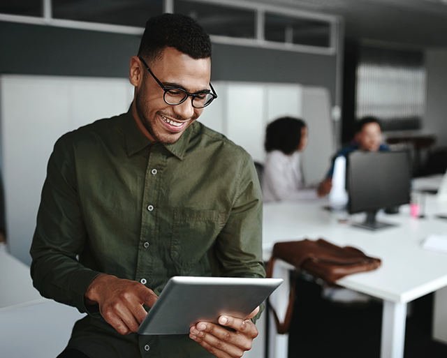 Man is smiling while looking at the tablet in the office